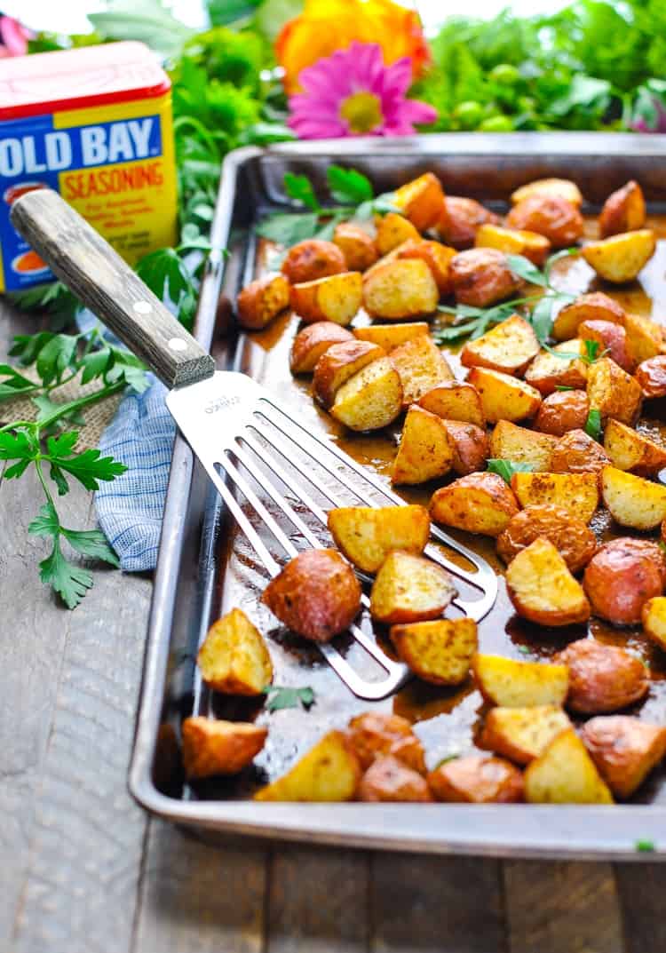 Crispy baked seasoned red potatoes in a roasting pan with a spatula