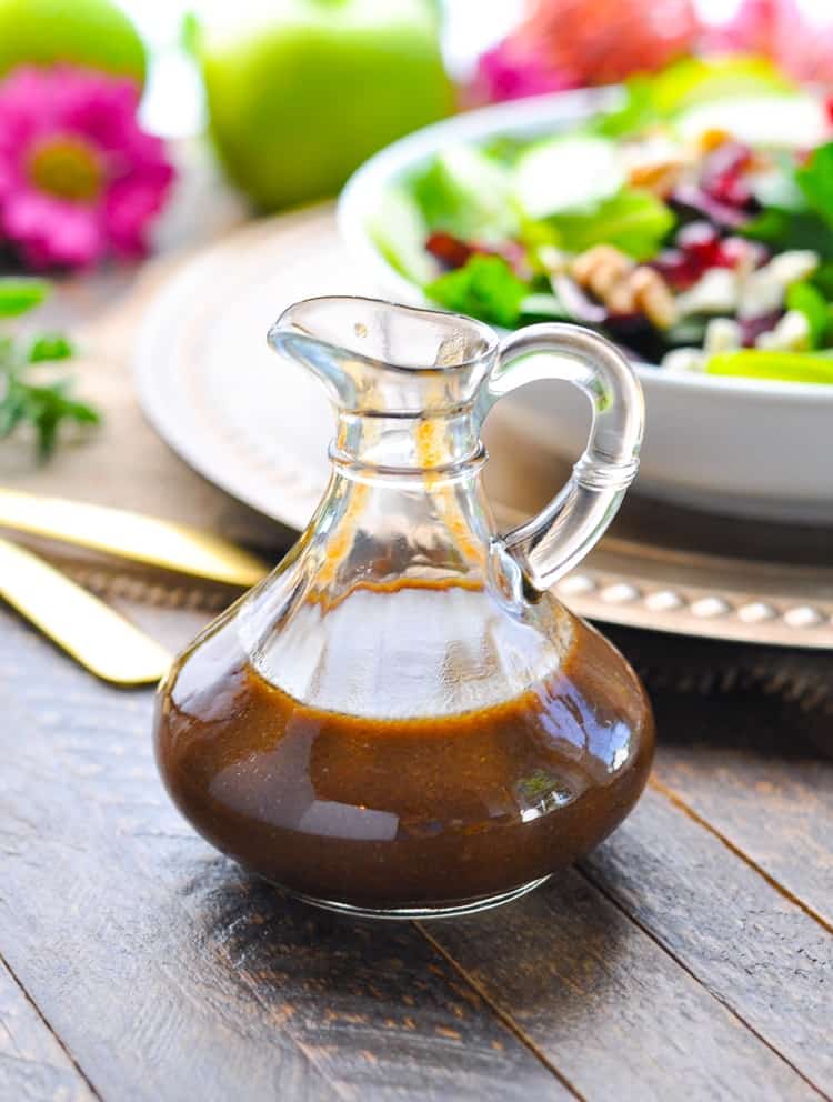 A close up of apple butter vinaigrette in a glass bottle ready for drizzling over a tossed salad