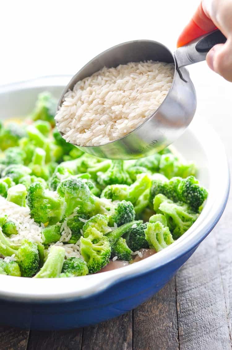 Pouring rice on top of broccoli in a casserole dish to make chicken broccoli rice casserole