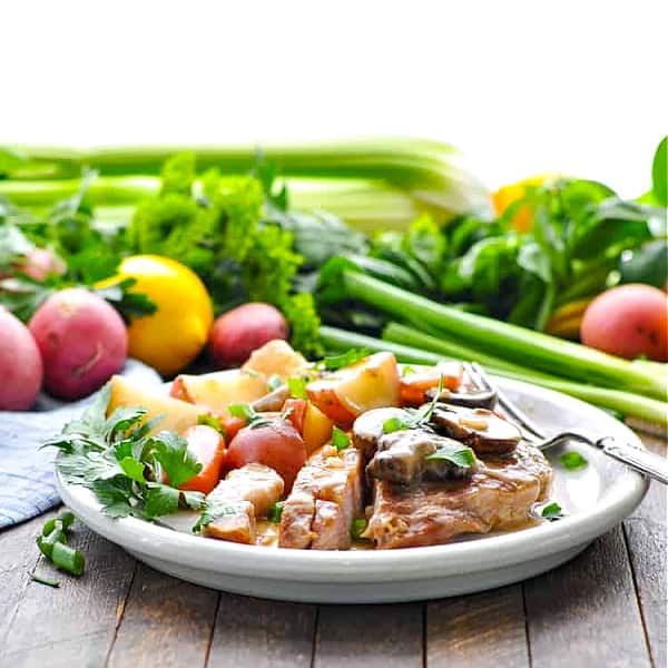 Square image of a plate of slow cooker pork chops with vegetables and gravy