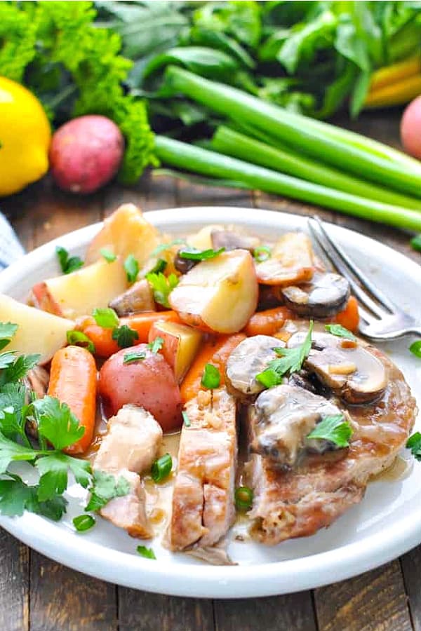 Front shot of slow cooker pork chops on a white plate with vegetables and gravy