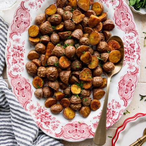 Square overhead shot of roasted seasoned potatoes on a red and white serving platter.