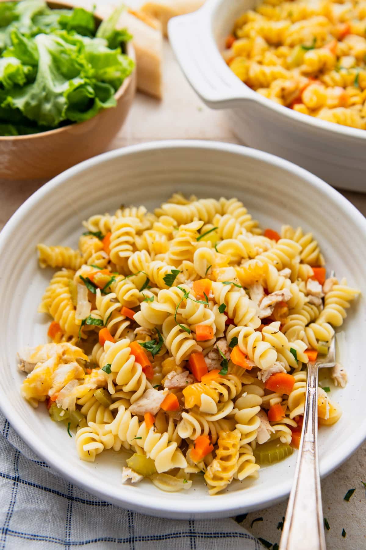 Side shot of a bowl of chicken noodle casserole served with salad and bread.
