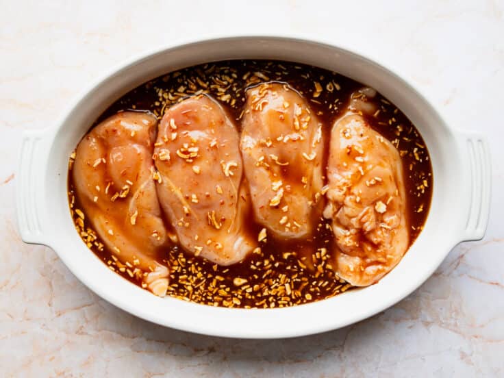 Pouring the sauce over the chicken in the dish before baking.