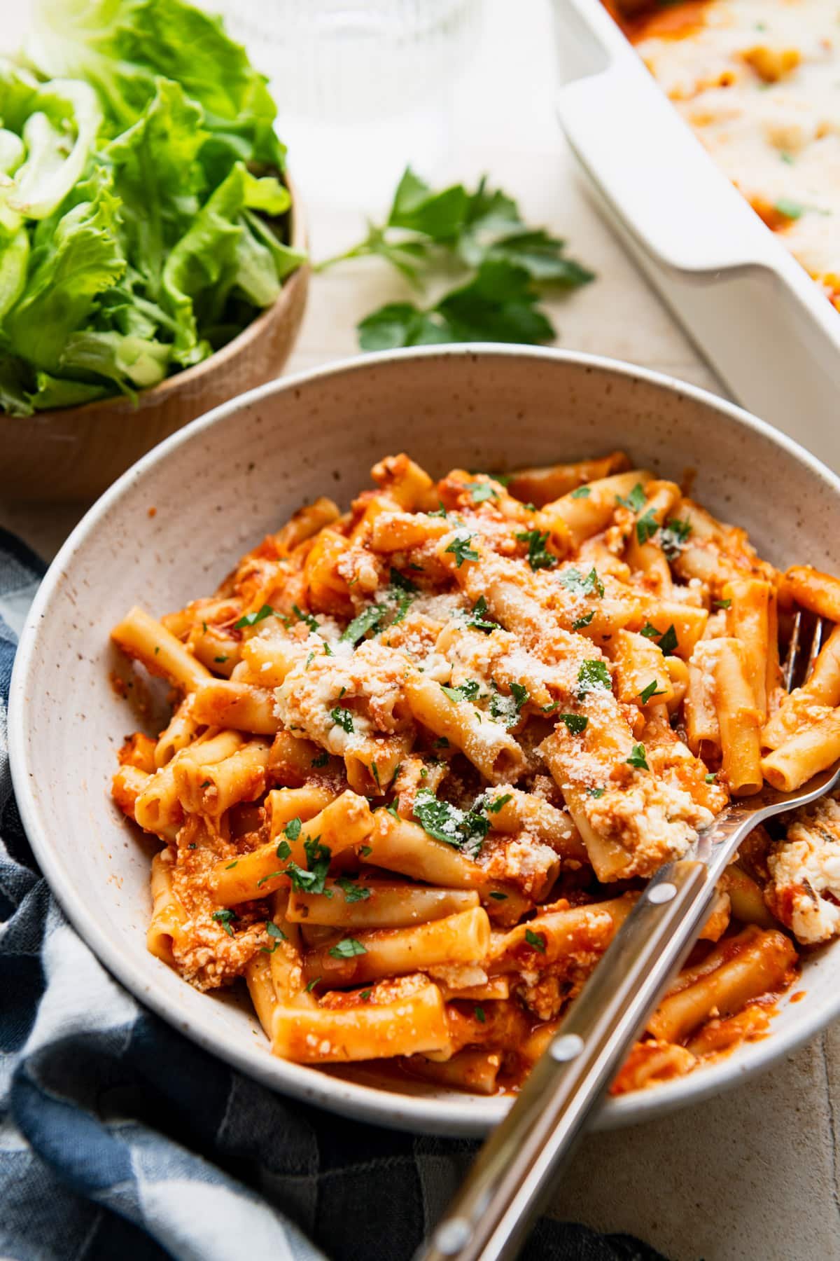 Side shot of a fork in a bowl of baked ziti.