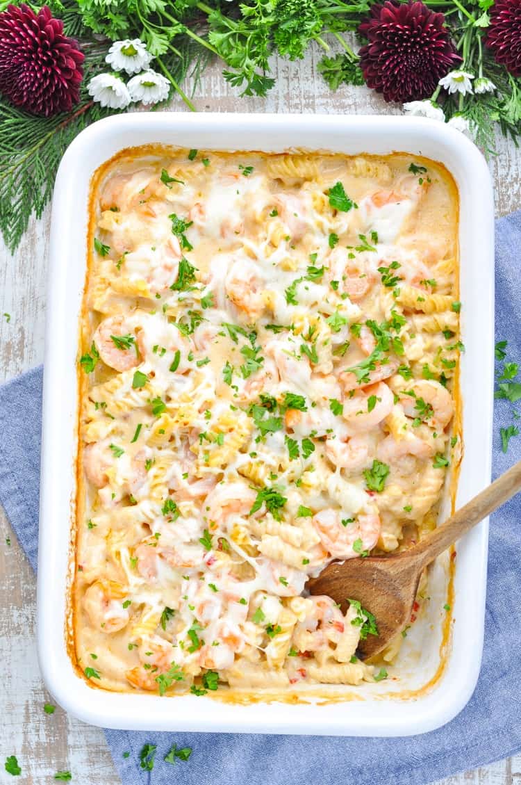 A white baking dish of creamy shrimp pasta with a wooden spoon in it