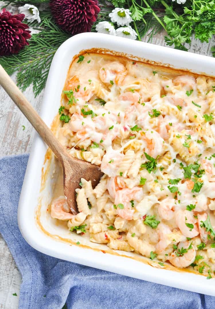 Creamy shrimp pasta in a white baking dish with a wooden spoon