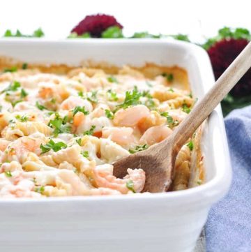A white casserole dish of creamy shrimp pasta topped with chopped parsley