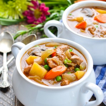 A beef stew in a white pot with carrots and potatoes