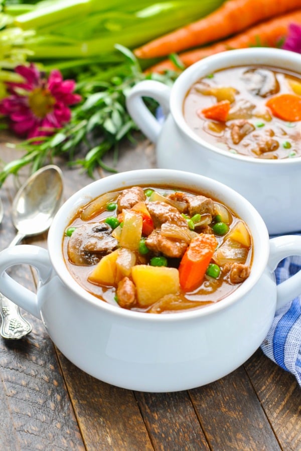 A slow cooker beef stew with red wine in a white bowl garnished with fresh parsley