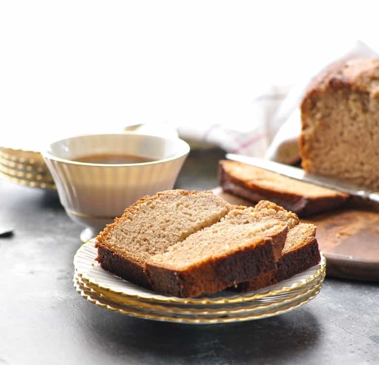 A slice of Amish friendship bread on a small plate with a cup of coffee in the background
