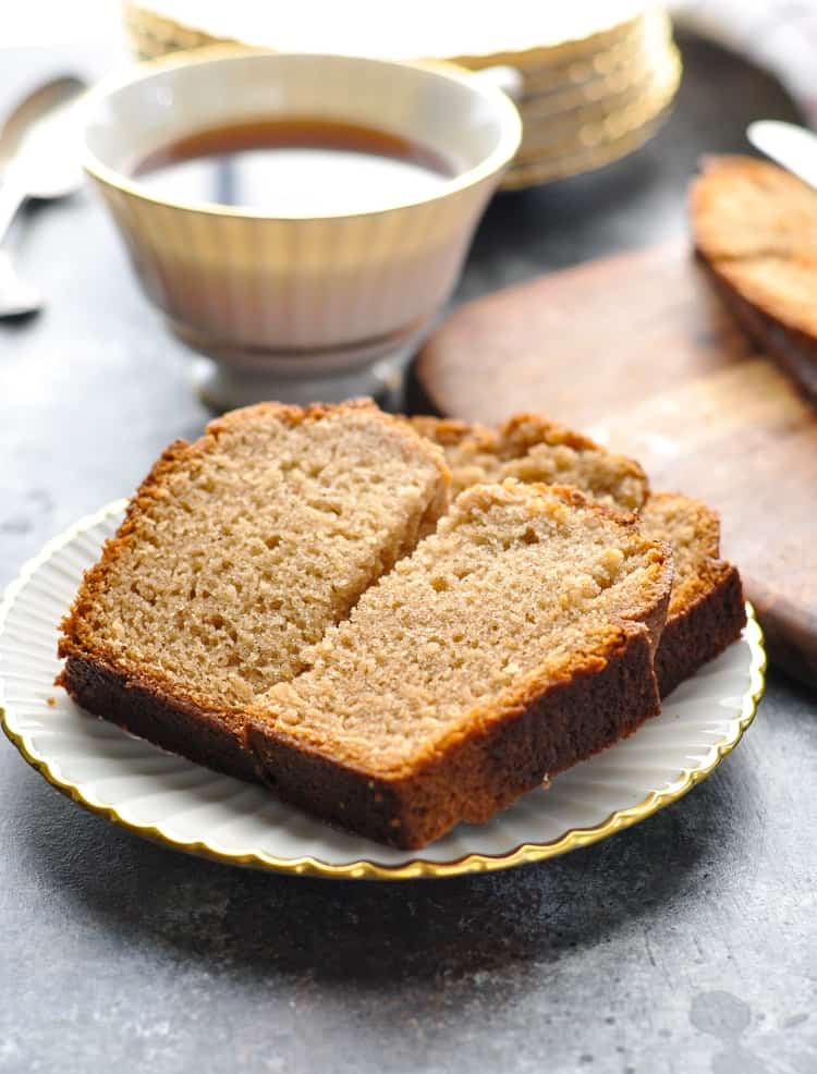 A close up of a slice of Amish friendship bread on a saucer with coffee in the background