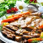 Sliced classic pot roast with potatoes and vegetables on a silver serving plate