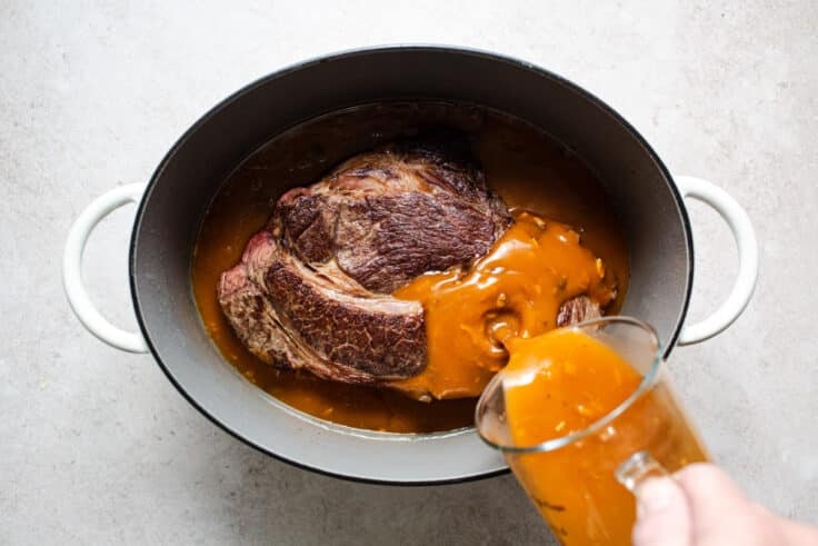 Adding the liquid ingredients to a slow cooker pot roast.