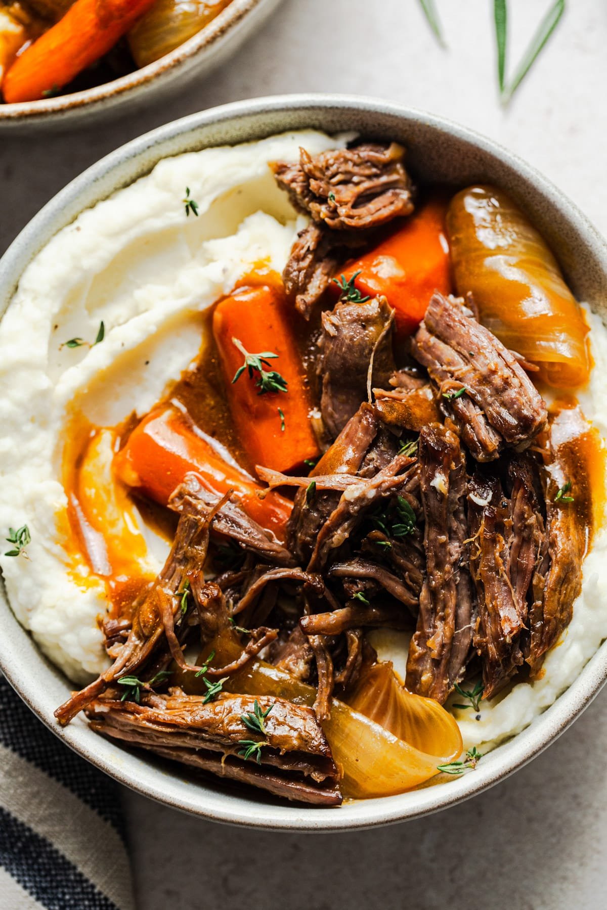 Close overhead image of a bowl of mashed potatoes topped with slow cooker pot roast and veggies.