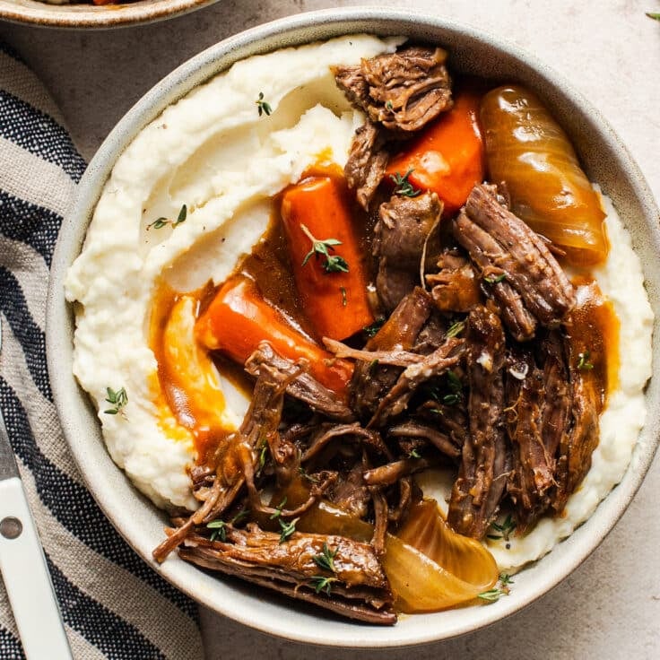 Square overhead shot of slow cooker pot roast with vegetables and gravy served over mashed potatoes.