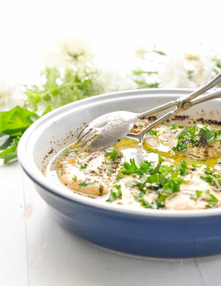 Bright photo of baked chicken breasts in a basil and white wine sauce.