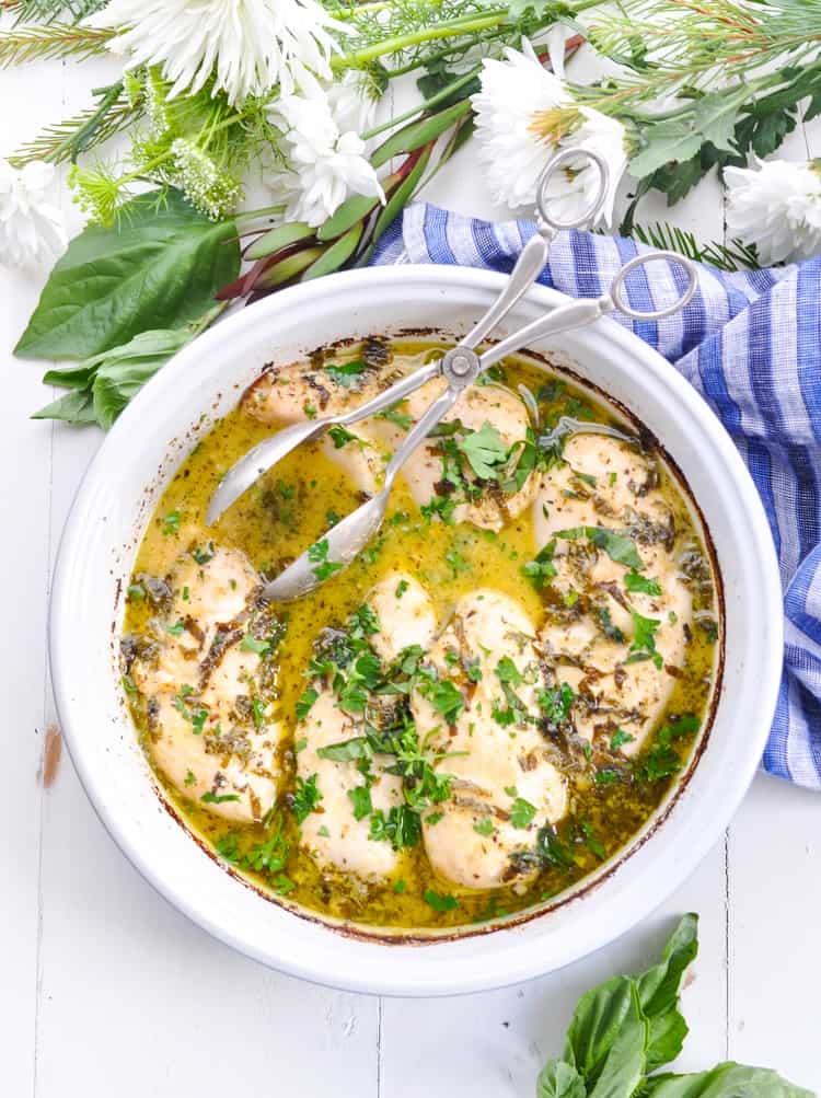 Overhead image of chicken breasts in a round casserole dish with fresh basil.