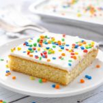 Slice of white texas sheet cake on a white plate with rainbow sprinkles