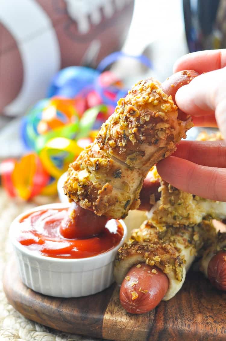 A hand dipping Jalapeno Pretzel Dogs in ketchup 