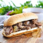 Photo of easy slow cooker French Dip Sandwiches on a wooden board with dipping sauce in the background