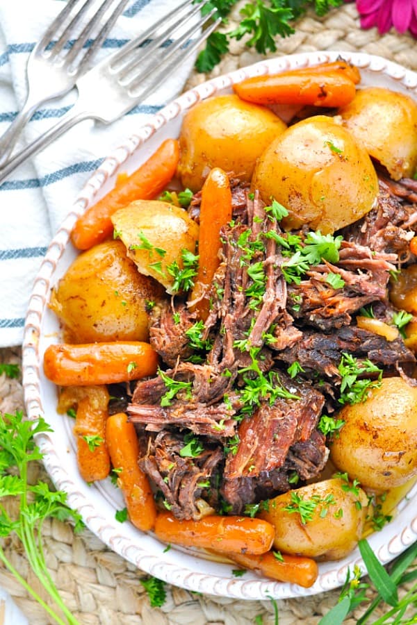 Long overhead image of a plate of a chuck roast recipe surrounded by potatoes and carrots