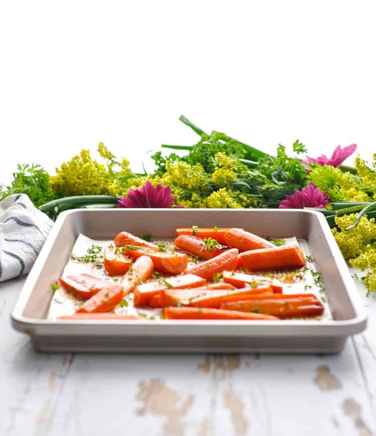 Baking tray of roasted carrot slices with flowers in the background