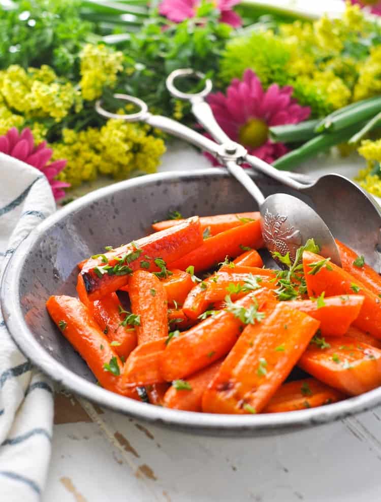 Bowl of brown sugar roasted carrots on a table with flowers