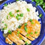 Overhead shot of baked bourbon chicken on a blue plate with rice and green onions