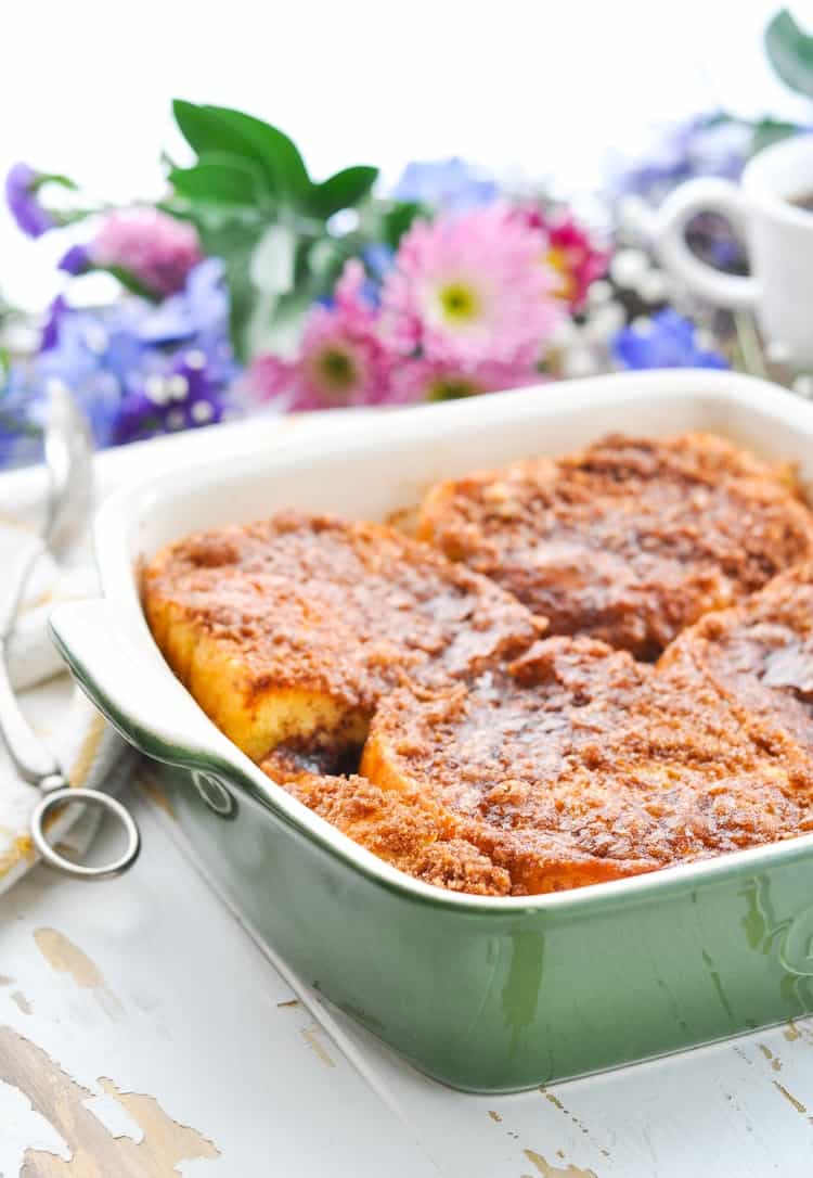 A side shot of an easy French Toast casserole in a green casserole dish with spring flowers