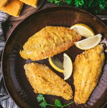 Close overhead shot of crispy fried catfish fillets in a cast iron skillet with lemon wedges and parsley