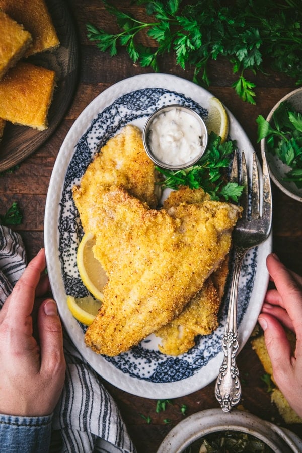 Hands holding a platter of crispy southern fried catfish.
