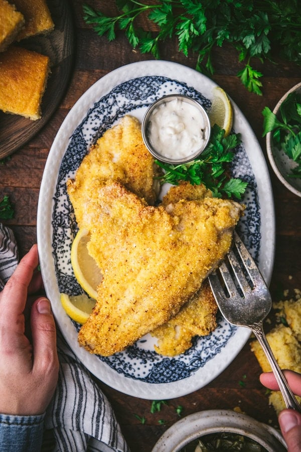 Hands serving fried catfish from a blue and white platter.