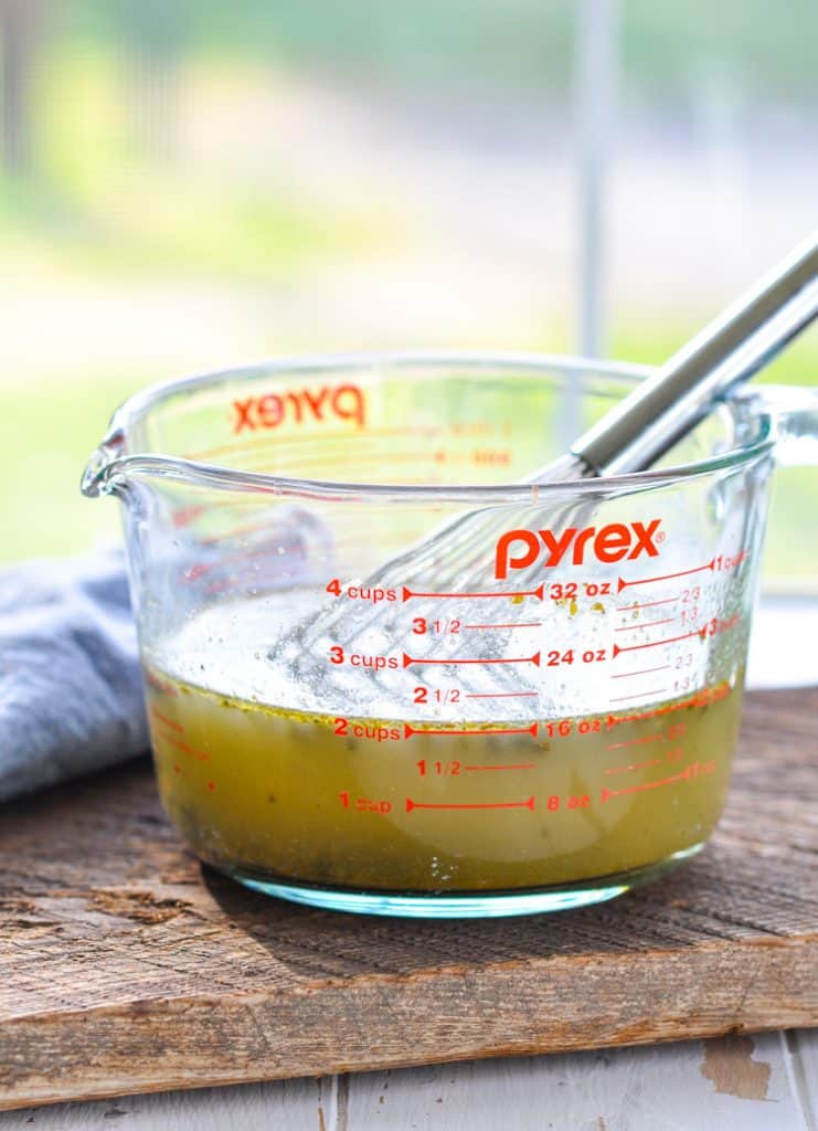 A large Pyrex glass measuring bowl filled with a pesto-chicken broth mixture for the dump and bake chicken pesto pasta.