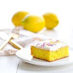 Lemon bar on a plate with lemons in the background