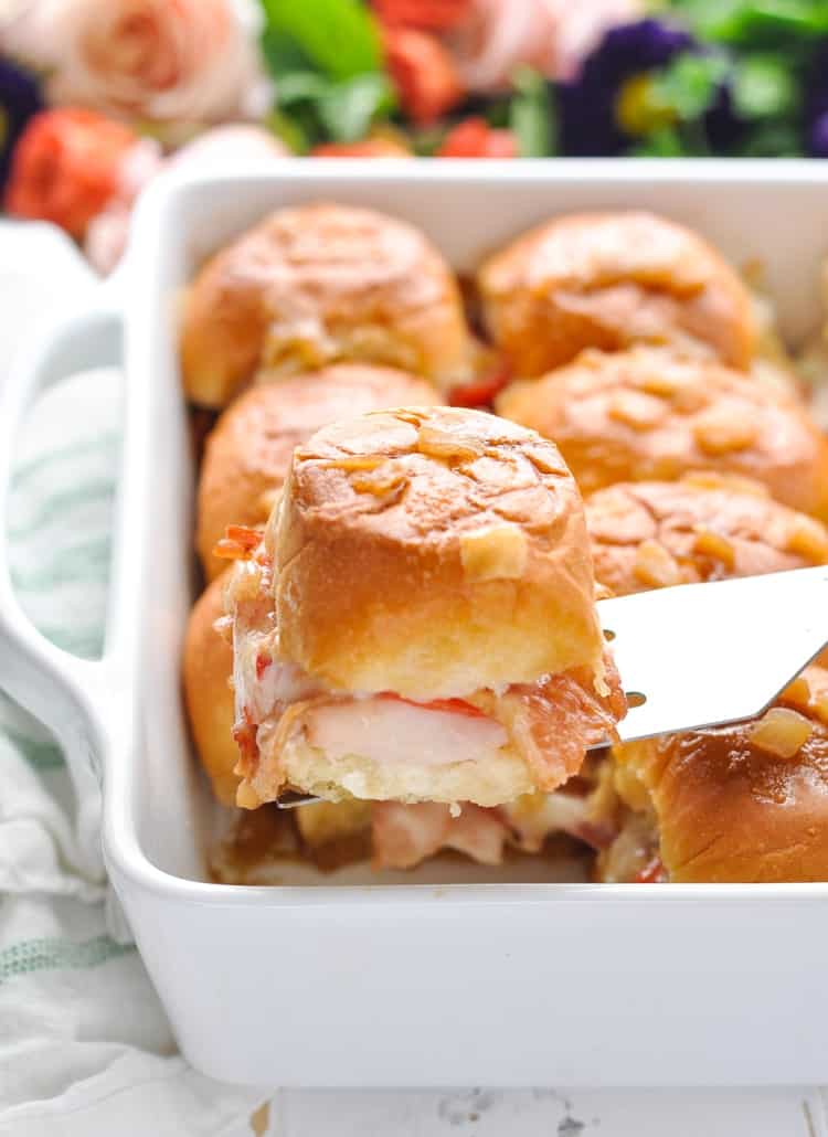 Close up photograph of Kentucky Hot Brown Sliders on a spatula in a casserole dish.