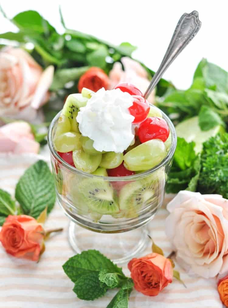 Photo of Mint Julep Fruit Salad in a glass dish surrounded by roses for a Kentucky Derby party.