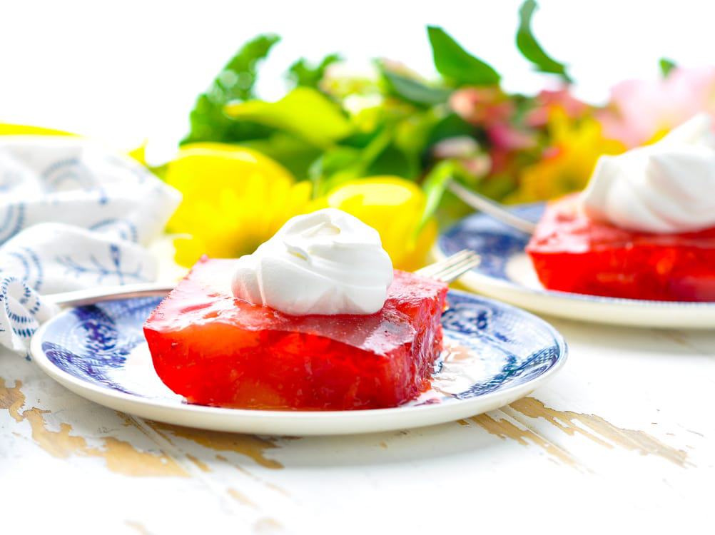 Slice of strawberry jello mold with whipped topping garnish.
