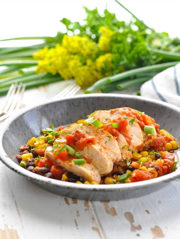 Enamelware dish with sliced salsa chicken over a bed of salsa corn and beans