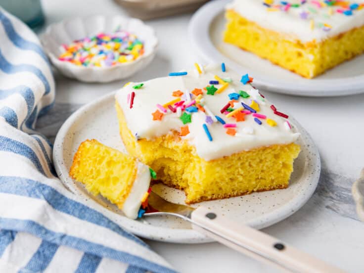 Horizontal side shot of frosted lemon bars with cake mix served on small white plates.
