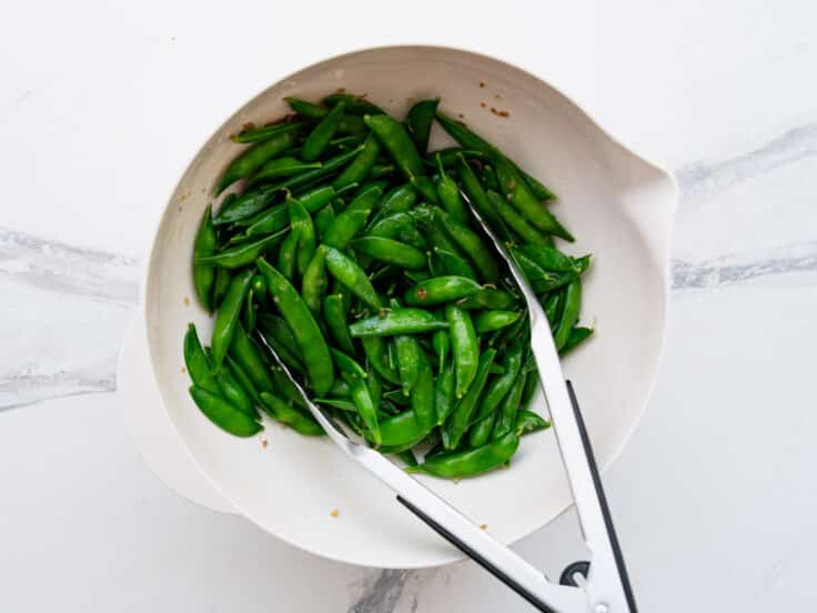 Tossing sugar snap peas with Italian dressing.