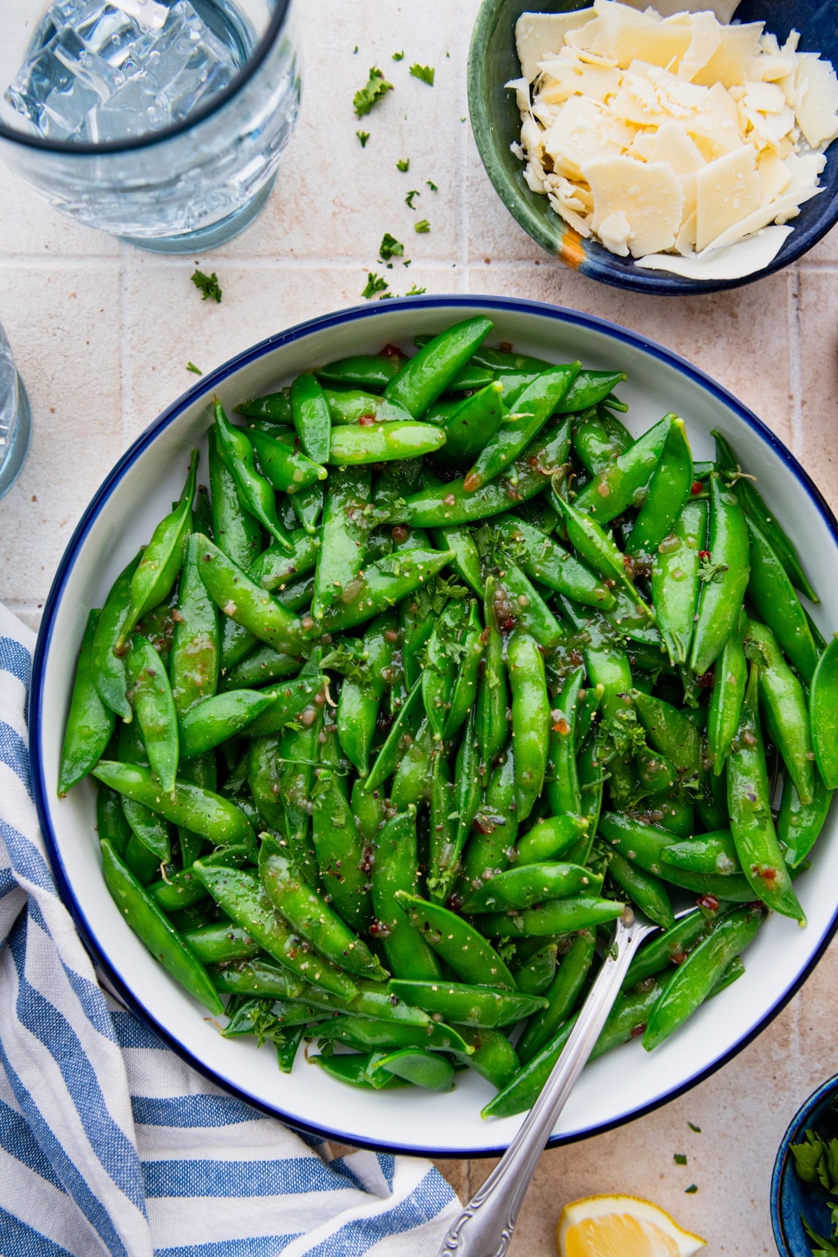 Overhead shot of the best sugar snap peas recipe served in a bowl with a side of shaved parmesan for garnish.