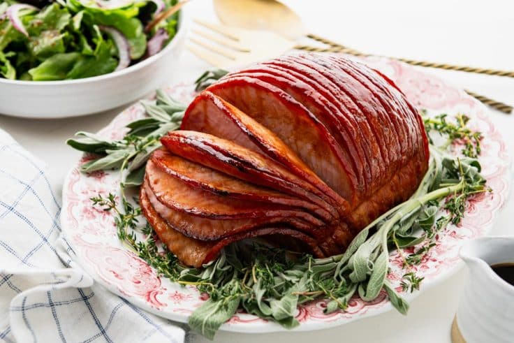 Horizontal side shot of a Virginia baked ham with brown sugar glaze served on a red and white vintage platter.