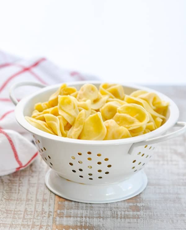 White colander with cooked tortellini sitting on a wooden surface