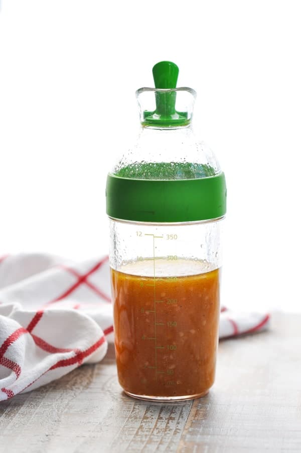 Bottle of homemade salad dressing for a tortellini salad sitting on a wooden surface