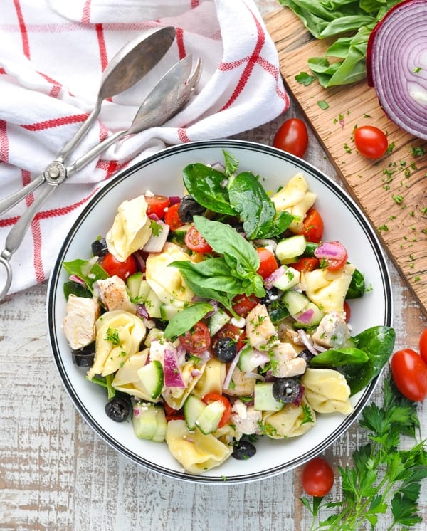Overhead image of a bowl of Mediterranean tortellini salad with chopped vegetables at the side