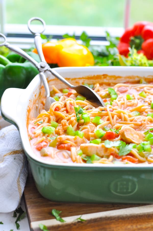 A close up image of a green and white ceramic casserole dish filled with a dump and bake baked spaghetti casserole topped with tomatoes and diced green peppers.