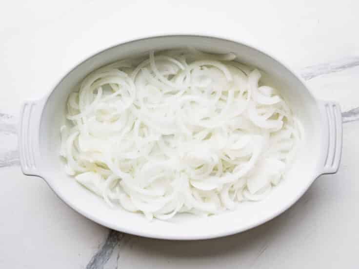 Sliced onions in the bottom of a white baking dish.