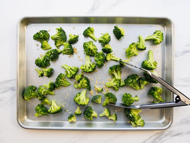 Tossing the raw broccoli florets on a sheet pan.