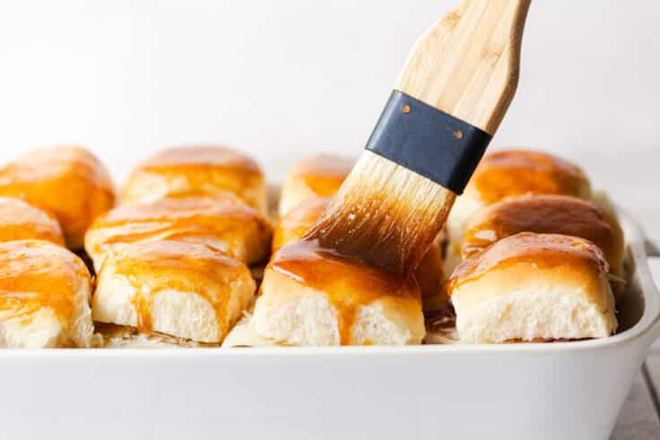 Brushing the tops of the rolls with the sweet garlic butter sauce.